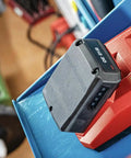 12V Li-Ion Battery Pack With Built-In Charge Indicator on red charger in workshop setting