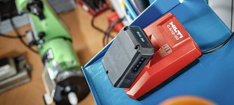 12V Li-Ion Battery Pack With Built-In Charge Indicator on red charger in workshop setting