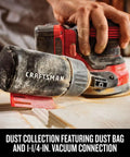 Hand using V20 Cordless 5 Inch Orbital Sander Bare Tool With 12,000 OPM on wood, showing onboard dust bag and vacuum connection