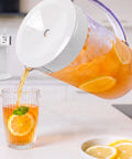 Generous 3 Quart White Stainless Steel Iced Tea And Cold Brew Coffee Brewing Pitcher pouring tea with lemon slices into a glass.