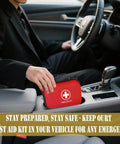 Person placing 196 Piece Waterproof Hard Shell Portable First Aid Kit For Home Car Camping Hiking Travel And Outdoor Adventures With Essential Medical Supplies In Red in a car cup holder.