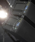 Audio speakers stacked at an angle with visible wires, set up in a dimly lit environment for a sound system installation.
