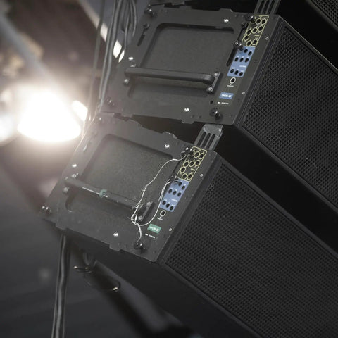 Audio speakers stacked at an angle with visible wires, set up in a dimly lit environment for a sound system installation.