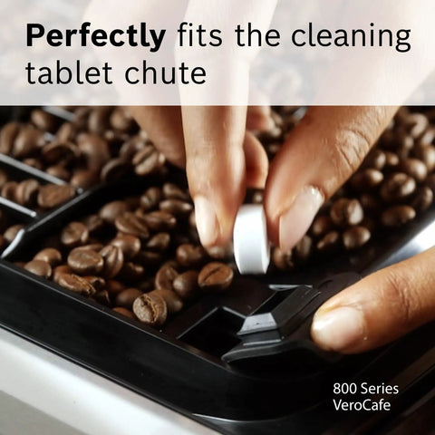 Hand placing VeroCafe Espresso Cleaning Tablet into coffee machine chute with coffee beans visible