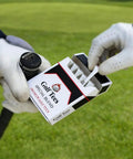 Person holding box of golf tees, labeled 'Premium Golf Tees,' on a green, featuring gloves and club handle.