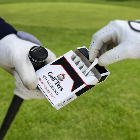 Person holding box of golf tees, labeled 'Premium Golf Tees,' on a green, featuring gloves and club handle.