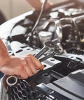 Front-view adjustable wrench in hand over car engine bay during auto repair.