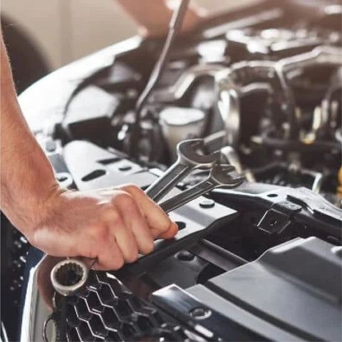 Front-view adjustable wrench in hand over car engine bay during auto repair.