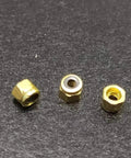 Three gold brass fingerboard lock nuts with nylon insert on a dark background, part of 24 Pack Gold Brass Fingerboard Lock Nuts With Nylon Insert, Bombproof Hardware For Upgraded Finger Skateboard Trucks, Legit Replacement Parts For Sick Tricks And Tight Rides.