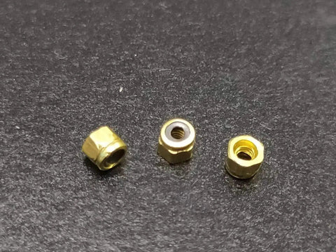 Three gold brass fingerboard lock nuts with nylon insert on a dark background, part of 24 Pack Gold Brass Fingerboard Lock Nuts With Nylon Insert, Bombproof Hardware For Upgraded Finger Skateboard Trucks, Legit Replacement Parts For Sick Tricks And Tight Rides.