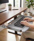 Heavy Duty Steel Under Desk Keyboard Tray Featuring Slick Ball Bearing Glides For Silky Smooth Extension And Rock Solid Ergonomic Workstation Support Up To Sixty Six Pounds With Zero Wobble Or Jamming Vibes with keyboard and hand in use.