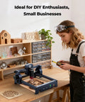 Person using Powerful 2500mW Laser Engraver With 130x130mm Work Area Ultra Fine 0.04mm Spot High Precision Laser Cutter And Engraving Machine For DIY Makers Free Software Included on a desk with crafts and tools nearby.