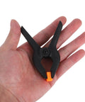 Super Durable Nylon Spring Clamps For Woodworking, Photography Setup, And Pool Cover Securing With Adjustable Grip Portable Clips Perfect For Crafts Backdrops. Black nylon spring clamp with orange tip held in hand