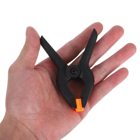 Super Durable Nylon Spring Clamps For Woodworking, Photography Setup, And Pool Cover Securing With Adjustable Grip Portable Clips Perfect For Crafts Backdrops. Black nylon spring clamp with orange tip held in hand
