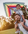 Father carrying child on shoulders flying rainbow kite at sunset