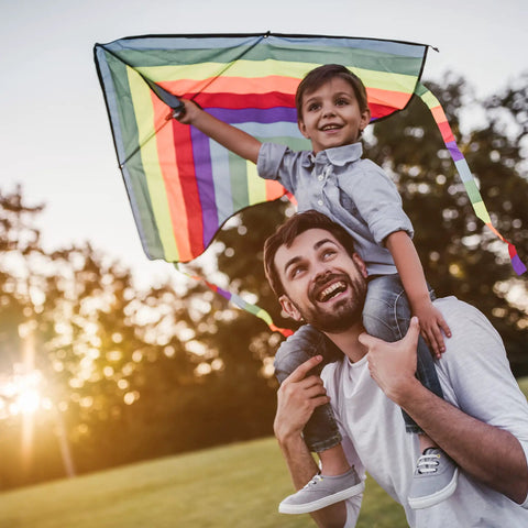 Father carrying son on shoulders flying a colorful kite in a sunny park