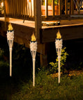 Natural Bamboo Tiki Torch Outdoor Set 2 Pack With Decorative Woven Design For Backyard Vibes And Garden Lighting Outdoor Parties Weddings Festivals Eco Friendly Oil Lamps installed in a garden