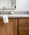 Antique brass cabinet knobs and handles on wooden bathroom vanity with sink and white towel, showing style and utility.