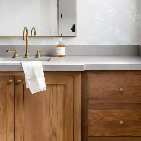 Antique brass cabinet knobs and handles on wooden bathroom vanity with sink and white towel, showing style and utility.