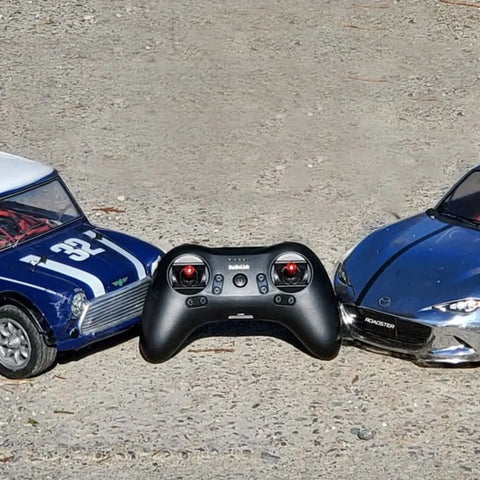 Compact 8 Channel 2.4GHz RC Transmitter With Built In Rechargeable Battery Pocket Size Dual Mode Controller shown between two cars