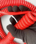 Straight Up Heavy Duty Stretch Coiled Extension Cord With Hella Tough Polyurethane Jacket And Flexible Spring Design That Kills Tangles And Delivers Clean Power Indoors Or Outdoors For Fifteen Meters held in a gloved hand.