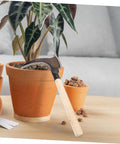 Do-It-All Manganese Sickle Garden Tool With Detachable Handle leaning against a potted plant, showcasing the sturdy blade and wooden handle.