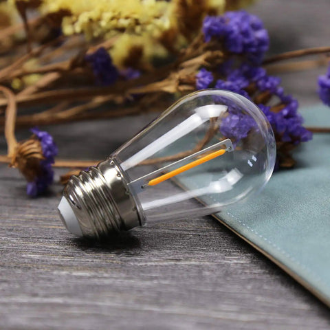 25 Pack Shatterproof S14 LED Replacement Bulbs For Outdoor String Lights One Watt Equivalent To Ten Watt Warm White 2200K Old School Edison Glow Vintage Filament Style E26 Base Waterproof UL Listed, single bulb with clear filament.