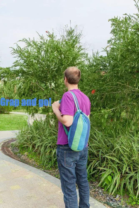 Person carrying a blue green striped pouch containing Extra Long And Wide Double Hammock For Travel Camping Backyard Porch Or Indoor Use