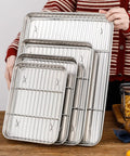 Person holding a set of Small Stainless Steel Serving Trays With Cooling Wire Racks Set 304 Grade, various sizes, shiny finish.