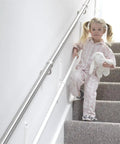 Fully Adjustable Toddler Stair Handrail Built Like A Tank For Little Ones Grows With Your Kid To Deliver Kid Approved Safety And Rock Solid Support Down Each Step Zero Hassle Standard Mount Kit with toddler in pajamas using handrail on stairs.