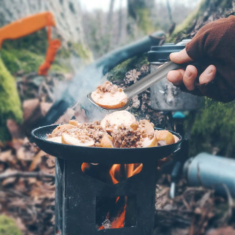 Hand using 4 Piece Titanium Long Handle Spork And Spoon Set Ultralight 8.4 Inch Flatware for camping, serving food over campfire.