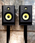 Dual ROKIT 7 G4 7 Inch Powered Studio Monitors with Kevlar Driver on Stands against a rustic wall