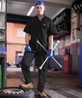 Lightweight Mens Short Sleeve Coveralls And Mechanic Work Jumpsuit Featuring Deep Cargo Pockets Woven From Breezy Summer Twill Cotton Blend For Tough Job Sites And The Daily Grind Low Key Comfy Shop Romper worn by man holding tools in a garage.