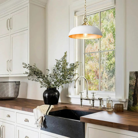 Top Shelf Matte White Farmhouse Pendant Light With Burnished Brass Accents above a kitchen sink with a dark stone counter.
