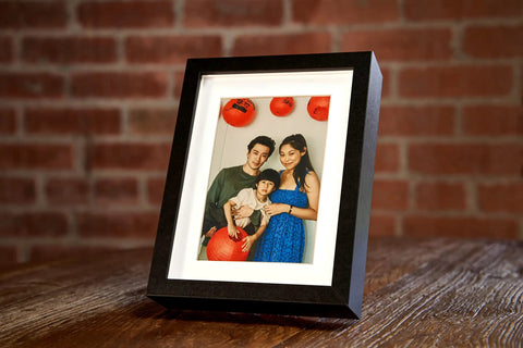 Photo Frame Diversion Safe With Hidden Compartment 4x6 Black Mini Safe Box on wooden table, showing family photo, brick wall background.