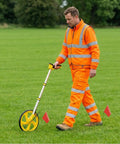 Sleek Digital Readout Distance Measuring Wheel With Heavy Duty Steel Roller And Crisp Backlit Display For Dead On Measurements And Quick Metric Or Imperial Swaps On Any Hustle Ready Job Site in use by contractor on grass.