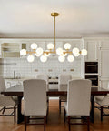 Mid Century Modern Sputnik Chandelier With 16 Lights Brushed Brass Arms And Frosted Milk Glass Shades For Kitchen Or Dining Room hanging above a dining table.