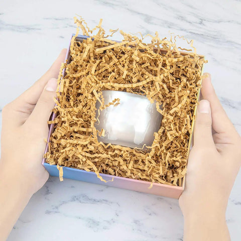 Hands holding a gift box filled with brown crinkle cut paper shred filler for gift baskets and boxes that looks great in gift sets