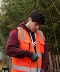 Person wearing High Visibility Safety Vest With Nine Pockets Zipper Closure Padded Neck And 360 Degree Reflective Strips ANSI ISEA Type R Class 2 Yellow Size Large For Construction Roadwork And Outdoor Jobs adjusting zipper outdoors.