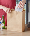 Person placing items in a 90 Pack Brown Kraft Paper Bags With Handles Bulk Assorted Sizes for shopping