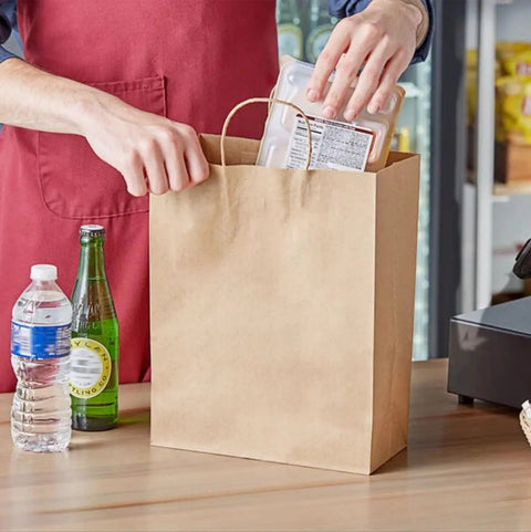 Person placing items in a 90 Pack Brown Kraft Paper Bags With Handles Bulk Assorted Sizes for shopping