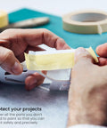 Person tearing a piece from the Six Roll Masking Tape Pack 0.75 Inch By 60 Yards Multi Surface Paper Tape For Painting Walls Glass And Sidewalk Chalk Art Delivers Clean Sharp Lines Leaves No Residue No Mess Easy Tear