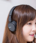Go Anywhere Plug And Play Wired On Ear Headphones With Snug Foam Tips And Sturdy Swivel Cups Built For Long Commutes And Chill Vibes In Classic Black worn by a woman.