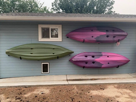 Big Time Heavy Duty 4 Pack Kayak Storage Racks Wall Mount Hangers For Canoe Paddleboard SUP And Snowboards Durable Steel Rack System holding green and pink kayaks on a blue wall.