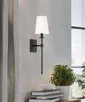 Dope Mid Century Modern Wall Sconce 20 Inch Tall With Oil Rubbed Bronze Finish And White Linen Shade Candle Style Wall Light for Bathroom or Powder Room Accent Lighting in a living room setting.