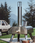 12 Inch Dual Fuel Outdoor Pizza Oven Portable Pellet And Gas Fueled Wood Fired Pizza Maker With Stone No Tools Needed Easy Switch Between Pellets And Gas Built In Gas Burner For Backyard Pizza Nights on a table in a grassy area