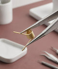 Close-up of golden stainless steel hair clip spring held by tweezers, part of 8 Pack Hair Clip Spring Replacement With Strong Clamping Steel Jaw Clips And Compact Body For DIY Hair Accessories Projects And Everyday Use Ideal For Crafting Hair Barrettes And Bobby Pins Durable Metal Spring Mechanism For Long Lasting Hold.