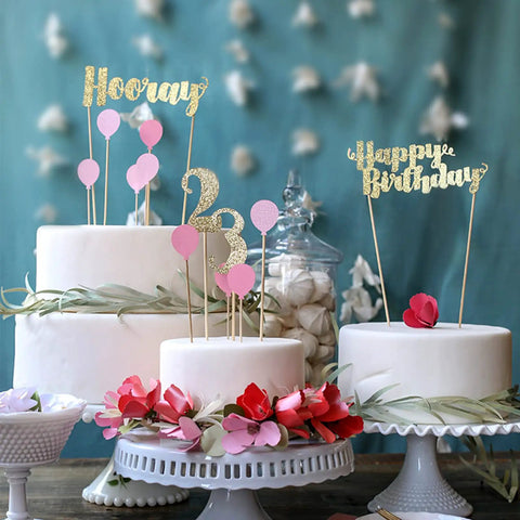Decorated cakes with gold and pink birthday toppers, featuring 'Hooray,' '23,' and 'Happy Birthday' in festive display.
