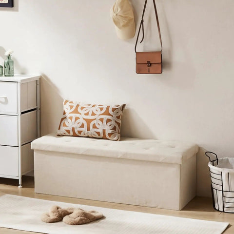 Foldable Storage Ottoman Bench With Padded Seat And Built In Chest in soft gray linen, placed in a bedroom setting.