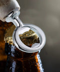 Close-up of a silver metal ring-style bottle opener prying a beer cap from a bottle